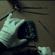 Someone with gloved hands carefully uses tweezers to pull out tape from a burned VHS cassette.